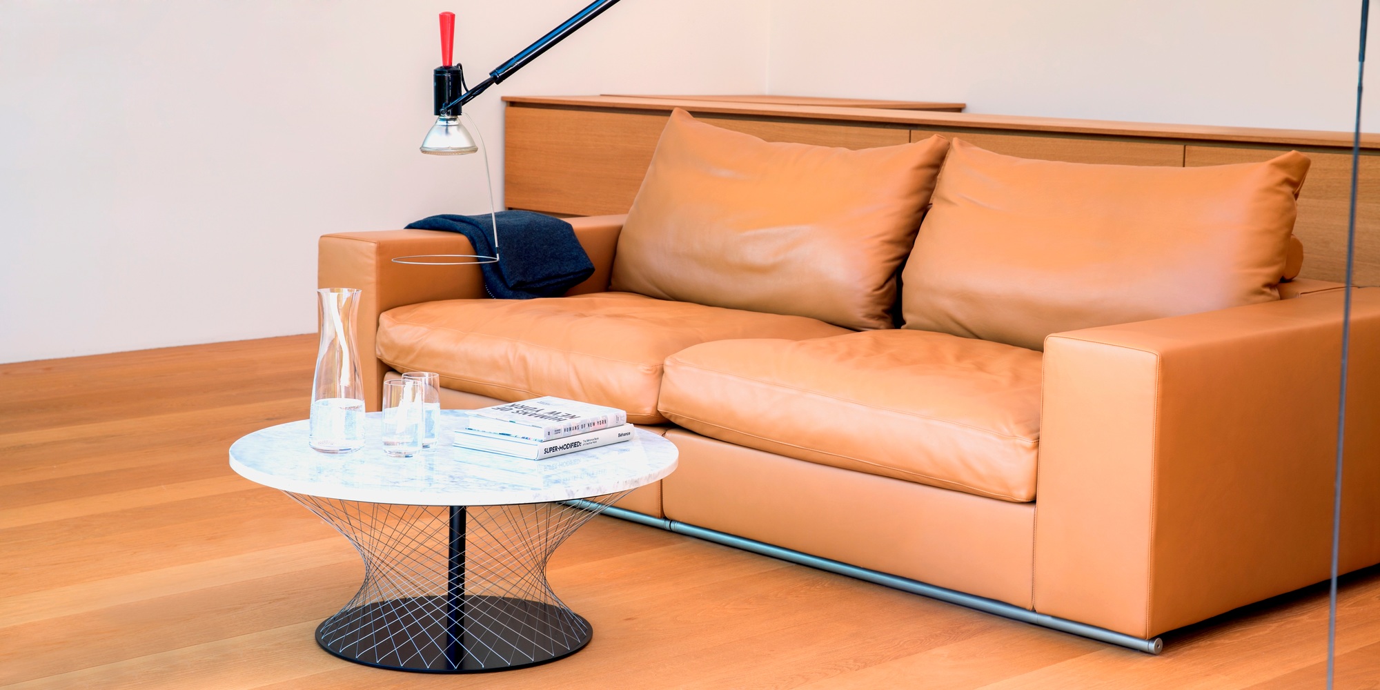 Eleganter Network Couchtisch Favius in Weiß mit Marmorplatte und Design-Drahtgestell neben Ledersofa.