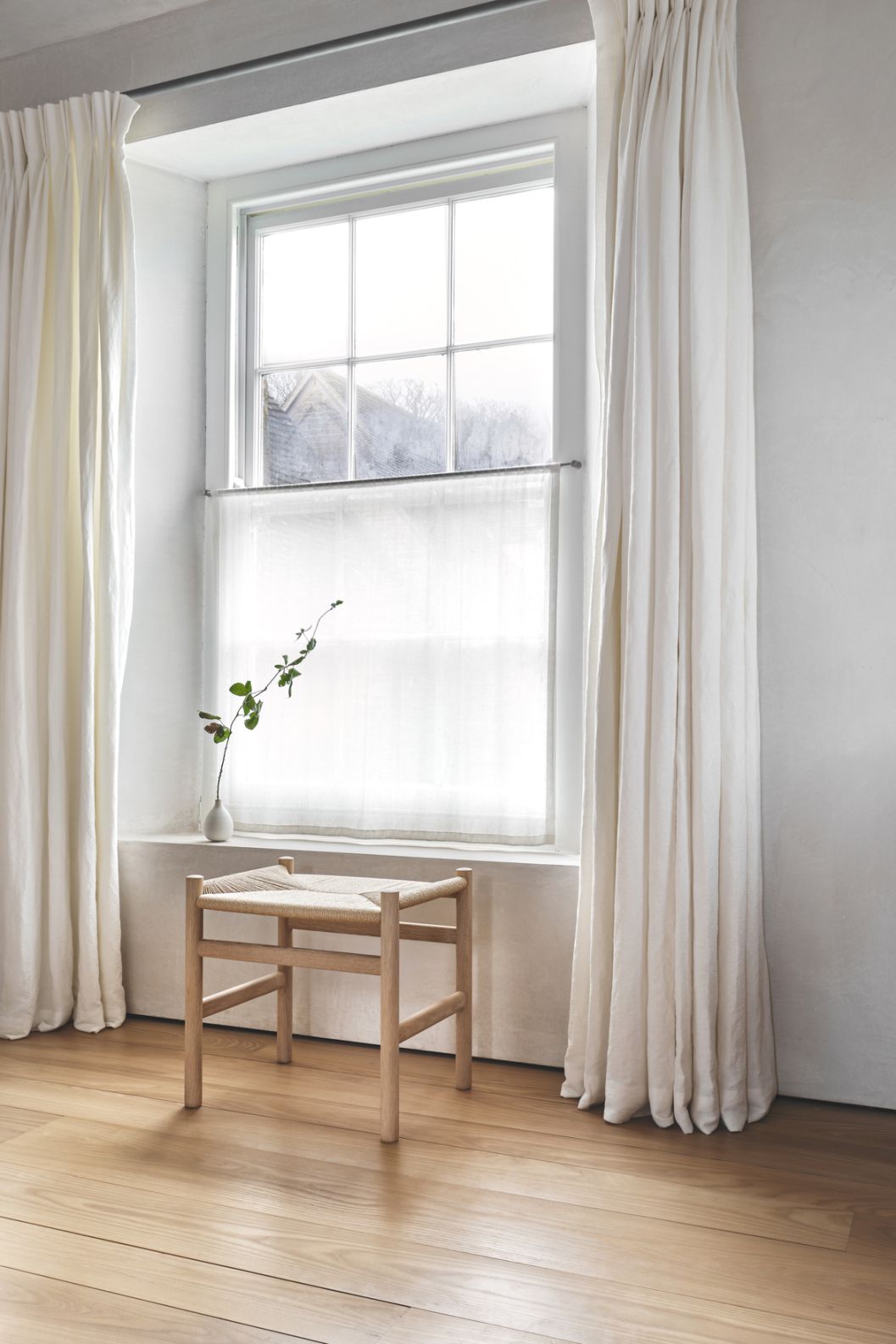 CH53 Hocker von Carl Hansen & Søn, Holzrahmen mit geflochtener Sitzfläche, vor Fenster.