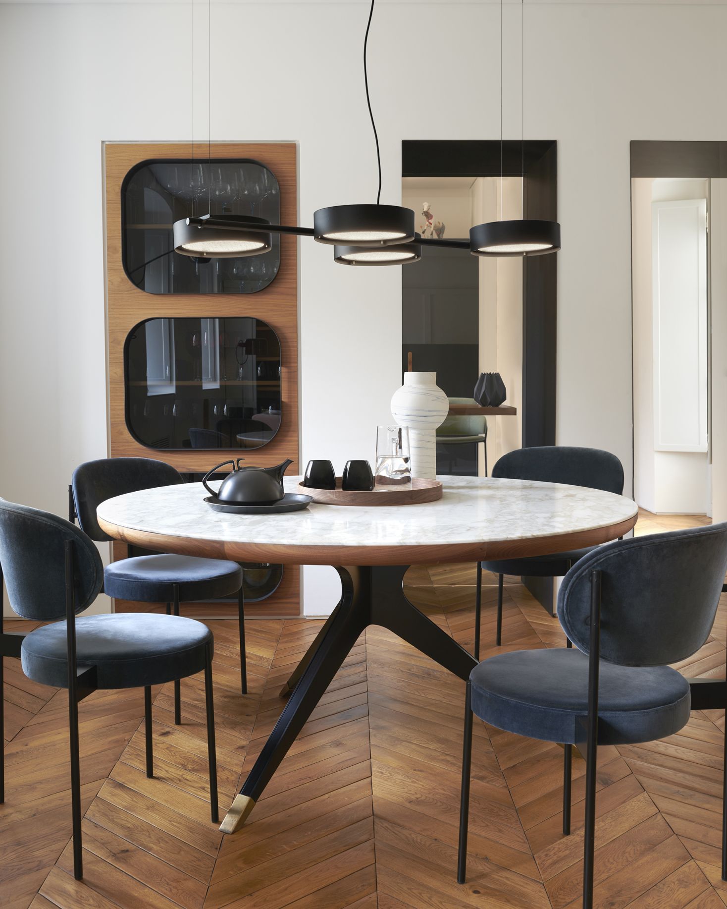 Esszimmer mit Berlin Hängeleuchte von Oluce, runder Tisch und blauen Stühlen.