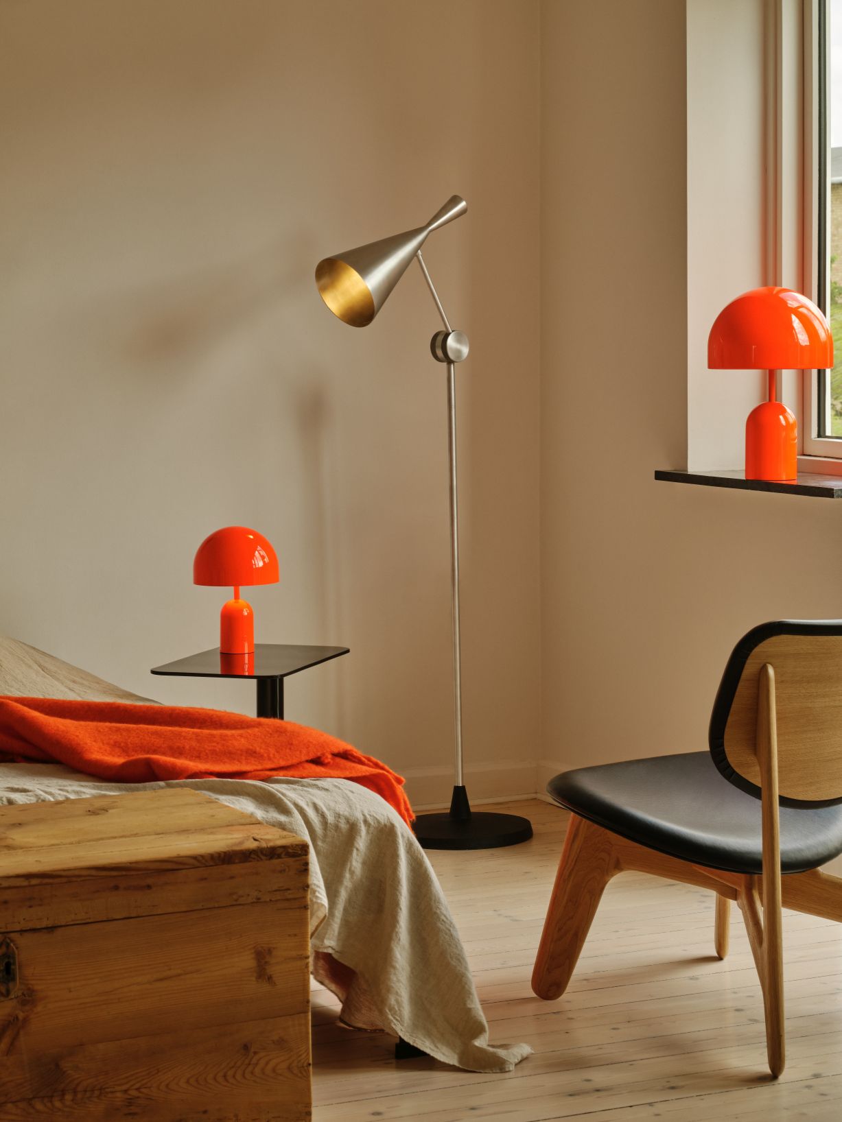 Moderne Unbeaten Stehleuchte von Tom Dixon im Schlafzimmer, ergänzt durch orangefarbene Tischlampen und einen Holzstuhl.