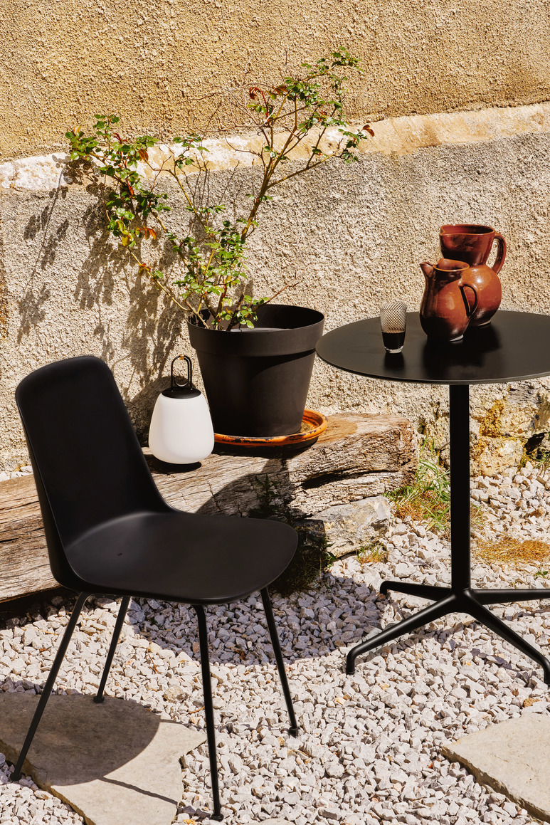 Schwarzer Rely HW70 Outdoor Chair Stuhl von AndTradition auf einer Terrasse mit Tisch und Dekoration.