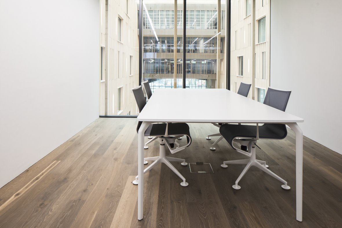 Heller Konferenzraum mit großem, weißen Tec Table Tisch und modernen Bürostühlen vor Fensterfront.