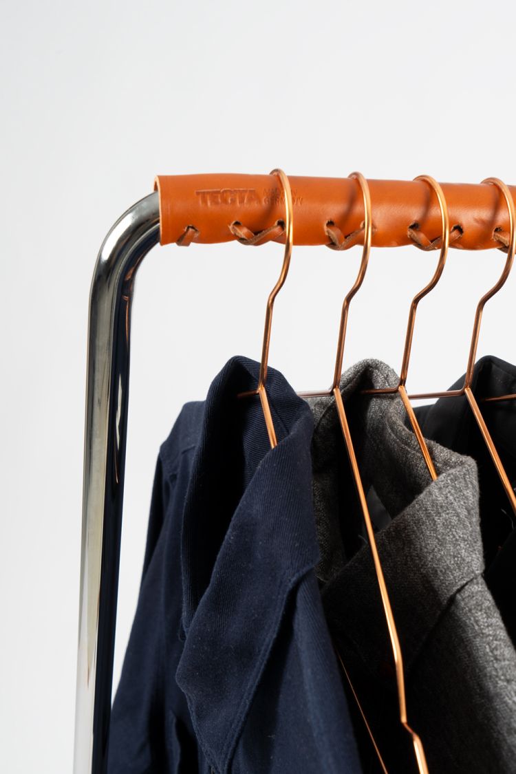 Detailaufnahme: Tecta Z10 Garderobenständer mit cognacfarbener Ledermanschette und Kleidung an Kupferbügeln vor neutralem Hintergrund.