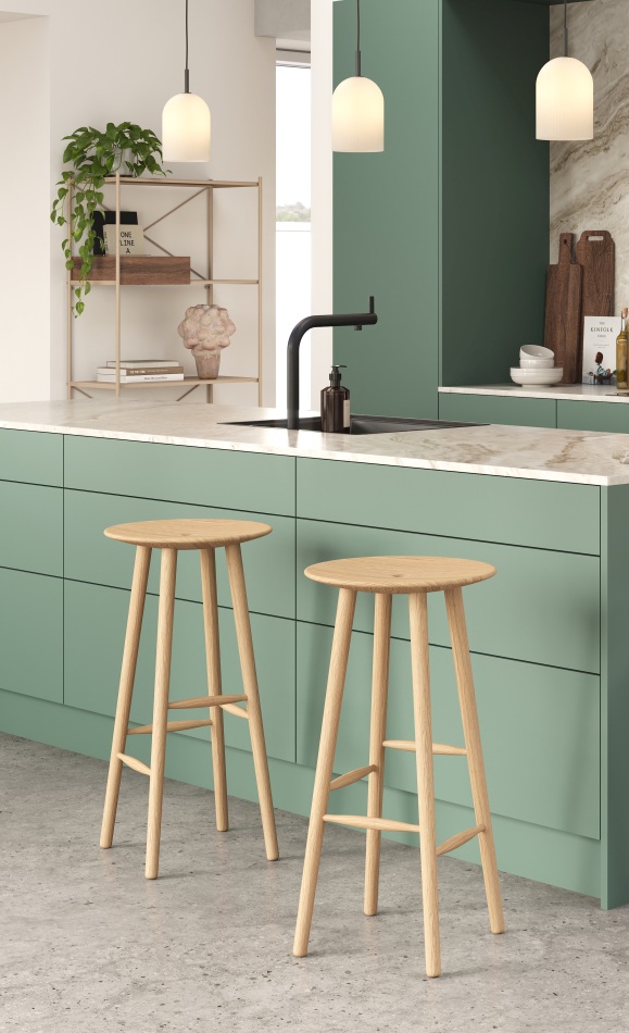 Zwei helle DI Volo Barhocker aus Eiche vor grüner Kücheninsel. Moderne Barstühle für Küche und Bar.