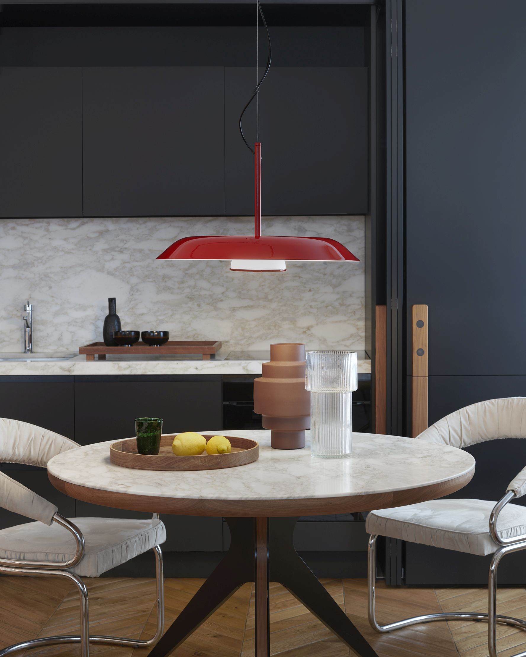 Rote Oluce Pendelleuchte Iride 879 über Esstisch mit Marmorplatte und Design-Stühlen.
