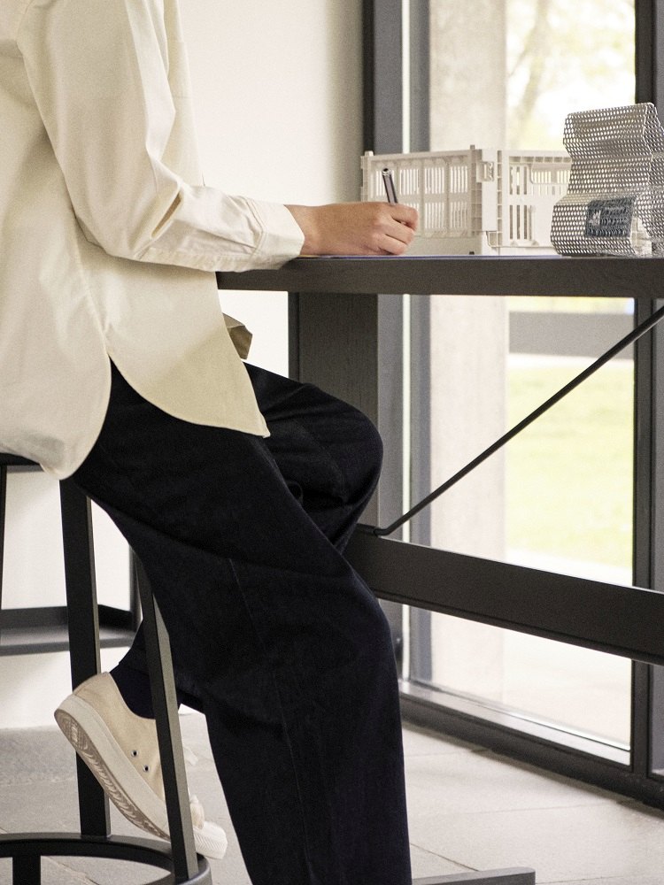 Person sitzt am Passerelle High Table Stehtisch mit schwarzem Gestell und arbeitet.