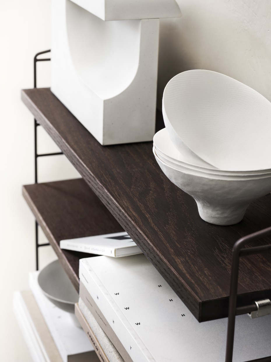 Nahaufnahme eines String Furniture Regalsystems mit dunklen Holzregalen und dekorativen Objekten.