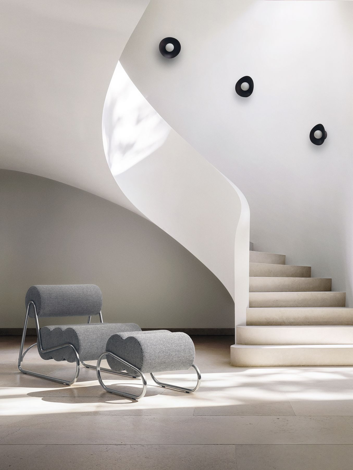 Grauer Fave Footstool Hocker von NORR11 mit Chromgestell vor einer Wendeltreppe in hellem Raum.