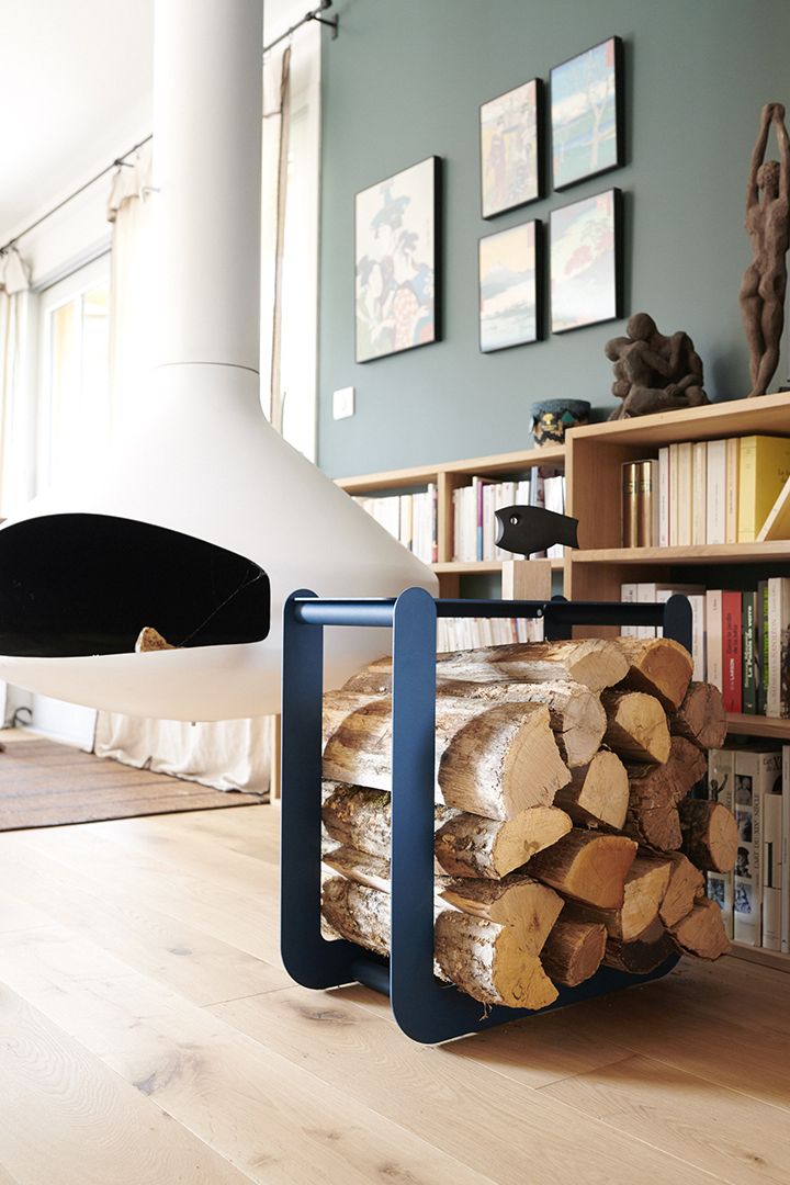 Nevado Holztrage von Fermob, gefüllt mit Brennholz, vor einem modernen Kamin und Bücherregal.