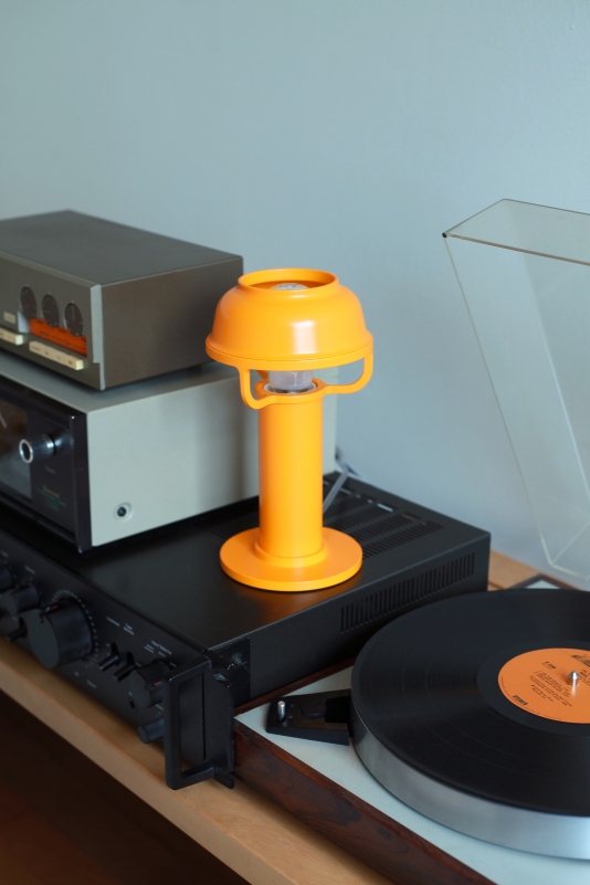 Orangefarbene Kori Tischleuchte von Artek auf einem Regal mit Hifi-Anlage und Plattenspieler.