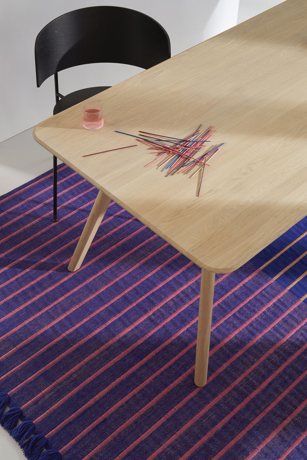 MEYER Tisch aus Holz mit bunten Mikado-Stäben auf einem gestreiften Teppich.