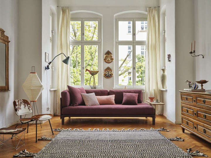 Wohnzimmer mit Vitra Anagram Panel Sofa in Bordeauxrot, stilvolles Möbeldesign und Teppich.