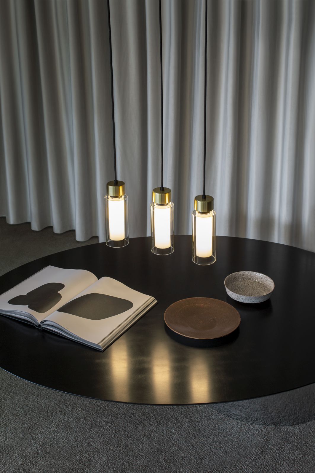 Osman Pendelleuchte von Tooy: Drei moderne Hängelampen mit Messing und Glas über einem Tisch.