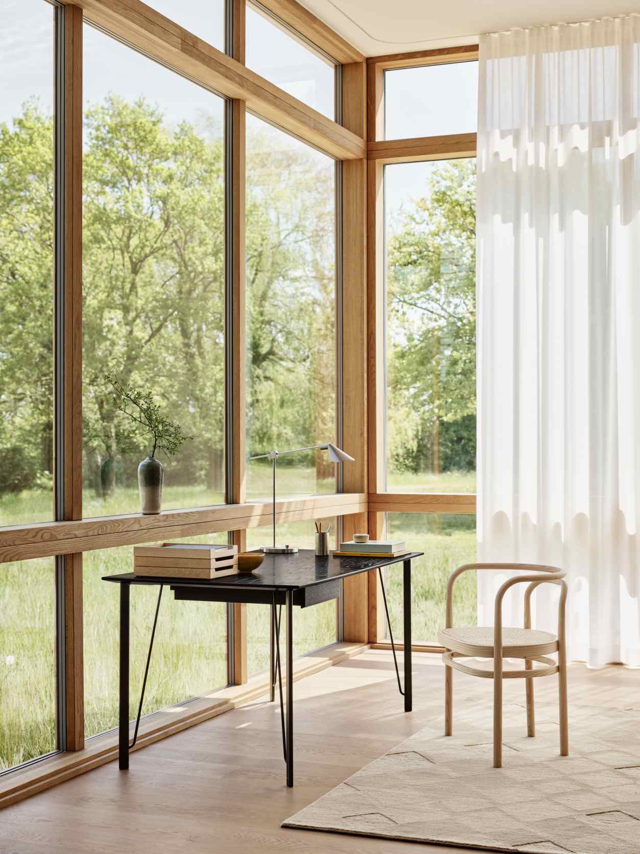 MS Series Tischleuchte von Fritz Hansen auf Schreibtisch in hellem Raum mit Fensterfront.