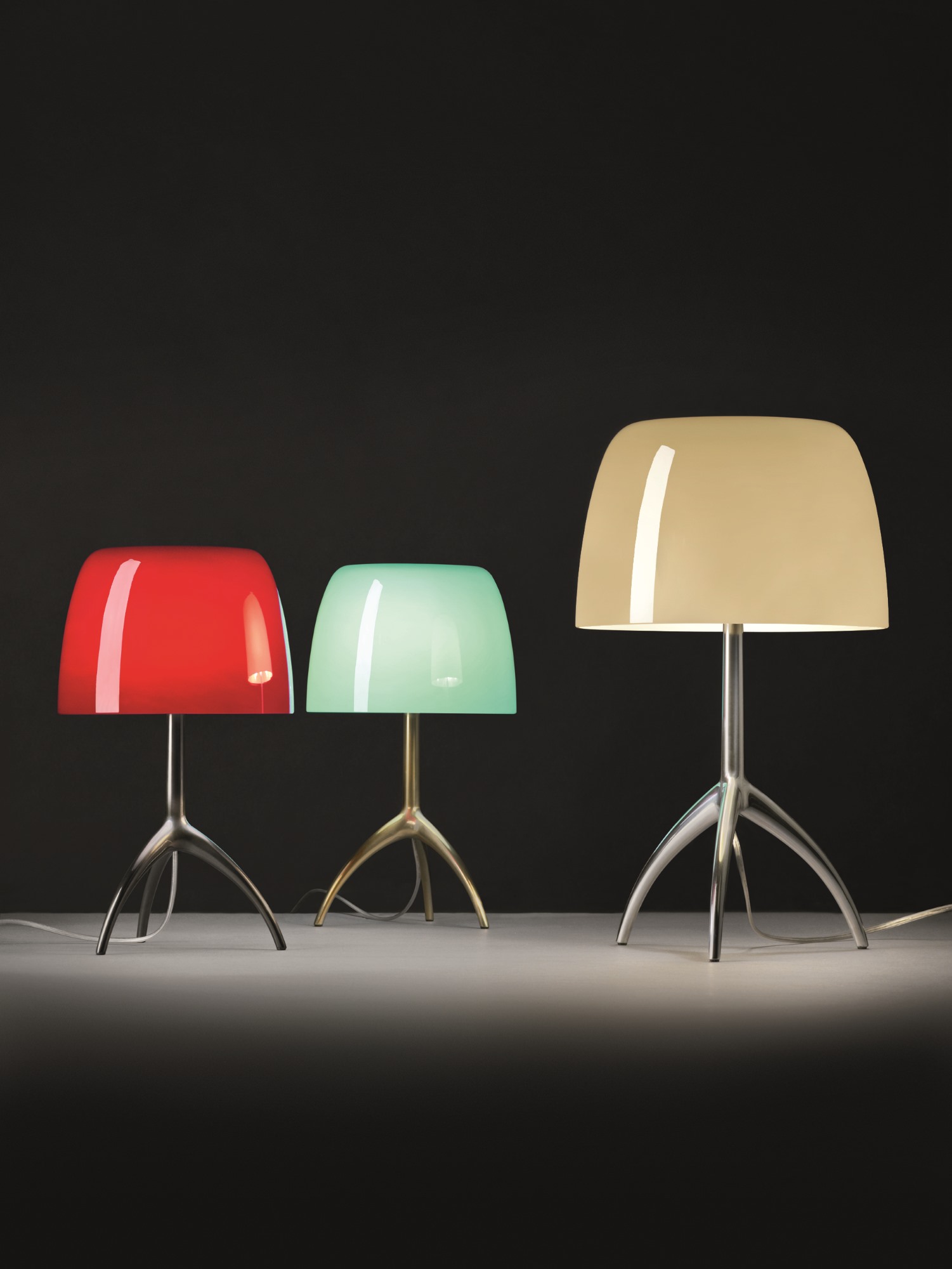 Drei Foscarini Lumiere Piccola Tischleuchten in Rot, Grün und Beige mit Stativfuß.