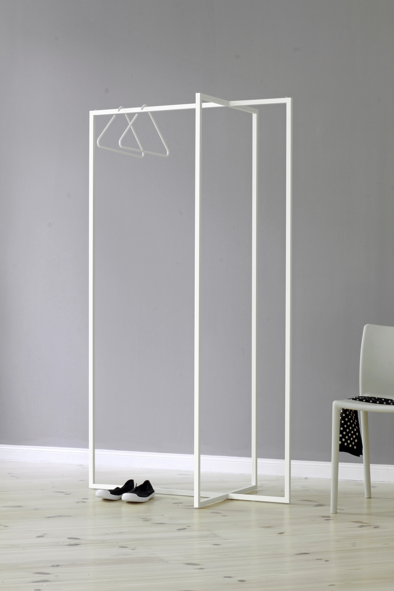 Weiße Modular Frames L Garderobe von Roomsafari mit Kleiderbügeln, Schuhen und Stuhl im minimalistischen Design.