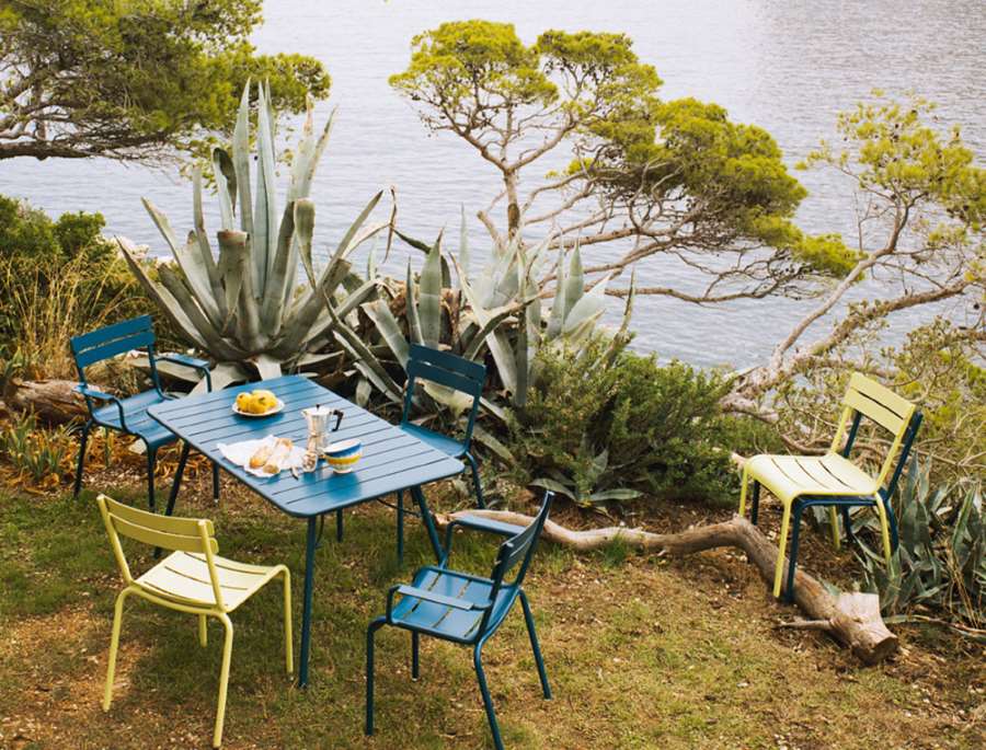 Blauer Luxembourg Gartentisch mit vier Füßen von Fermob, umgeben von Stühlen im Freien.