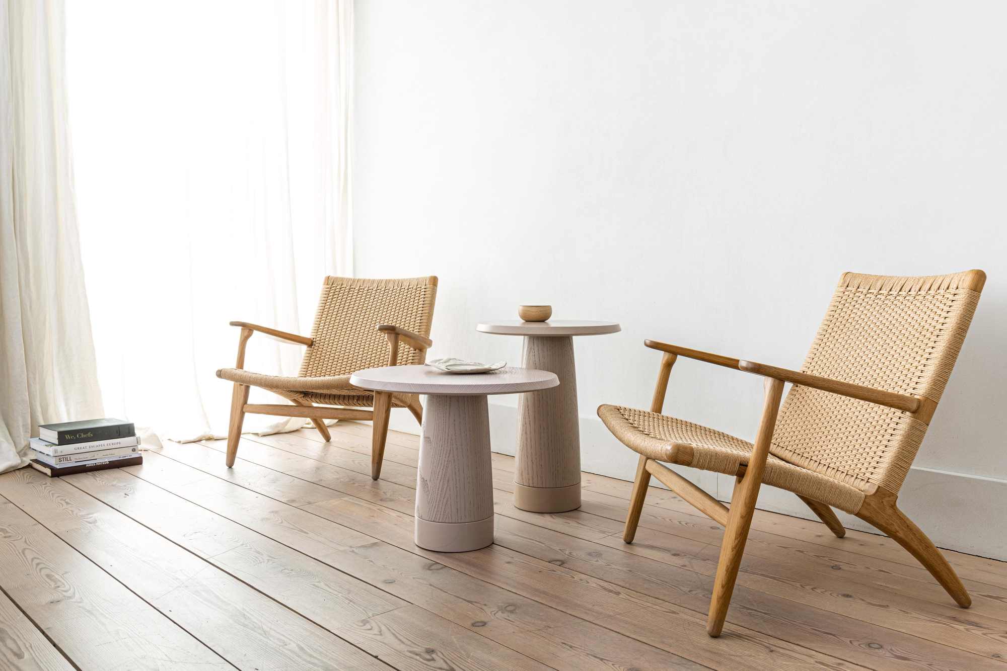 Zwei Amanita Beistelltische von Schönbuch zwischen zwei Korbsesseln auf einem Holzboden.