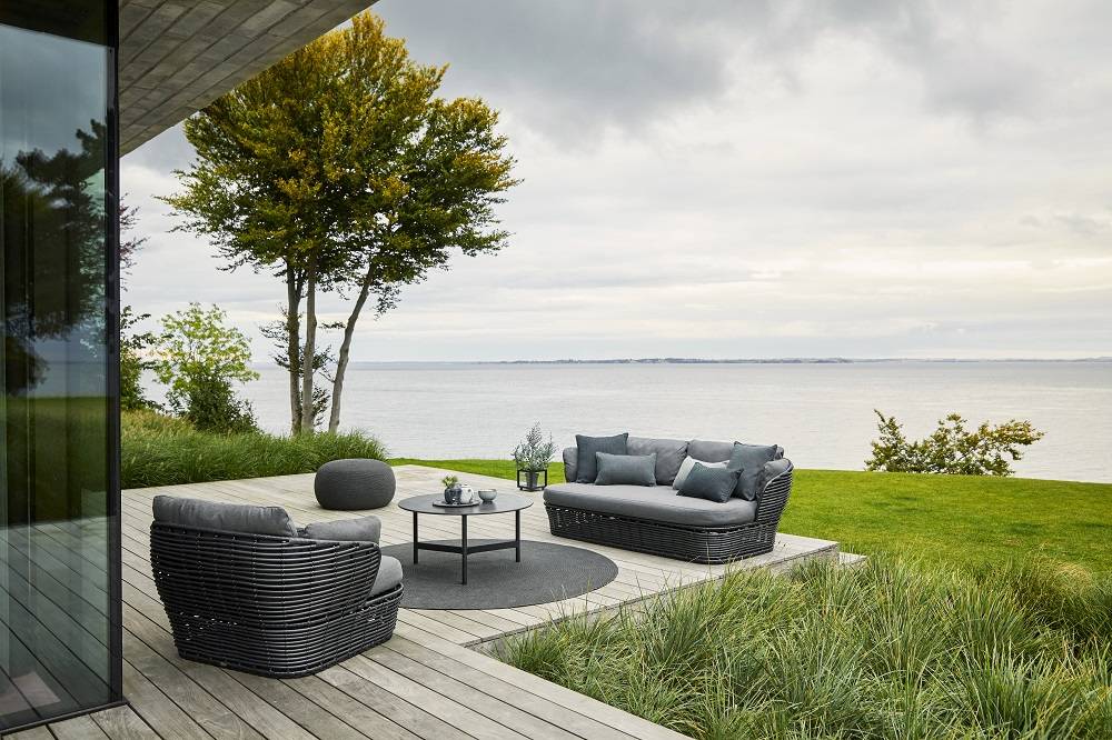 Basket Outdoor Loungesessel von Cane-Line mit graphitfarbenem Gestell und grauen Kissen auf einer Terrasse.