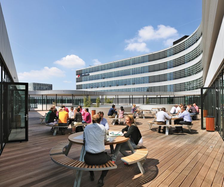 Menschen sitzen an Gargantua Picknicktischen von Extremis im Freien auf einer Holzterrasse.