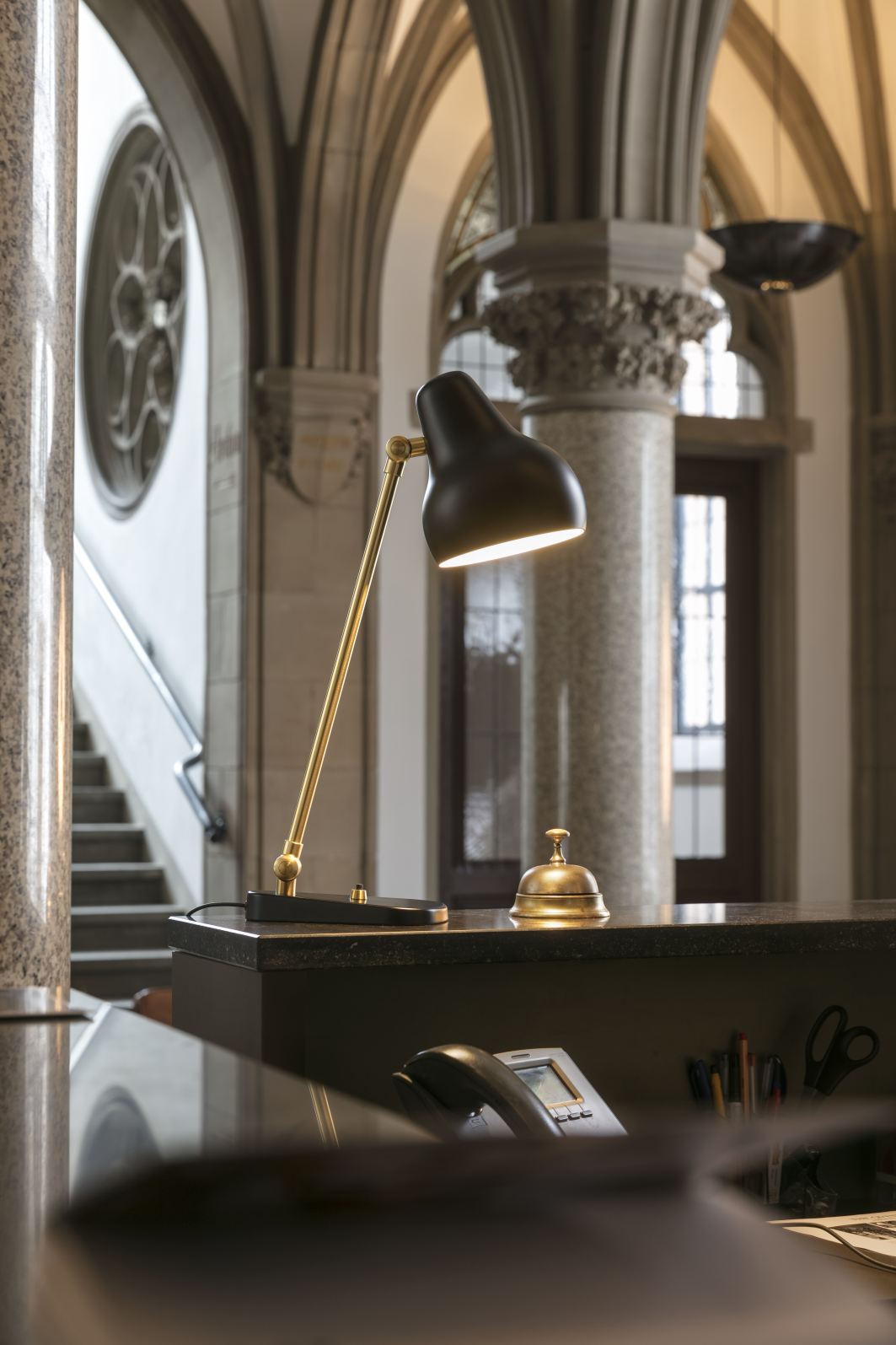 Nahaufnahme der VL38 Tischleuchte von Louis Poulsen in Schwarz und Gold auf einem Empfangstresen.