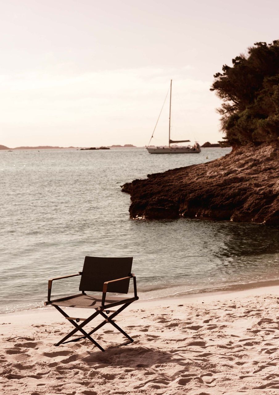 SeaX Armlehnstuhl von Dedon am Strand mit Meer und Segelboot im Hintergrund.