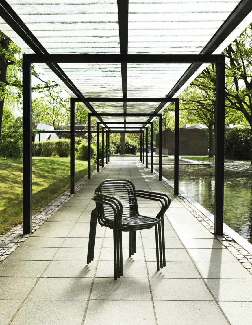 Normann Copenhagen Vig Armchair: Stapelbare Outdoor Armlehnstühle aus Metall in Grün unter einer Pergola.