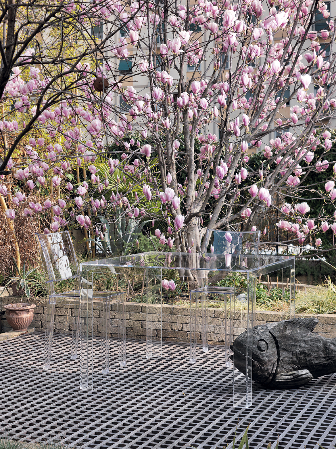 Transparenter Kartell Beistelltisch "Invisible Side" niedrig im Garten mit Stuhl und Deko-Fisch.