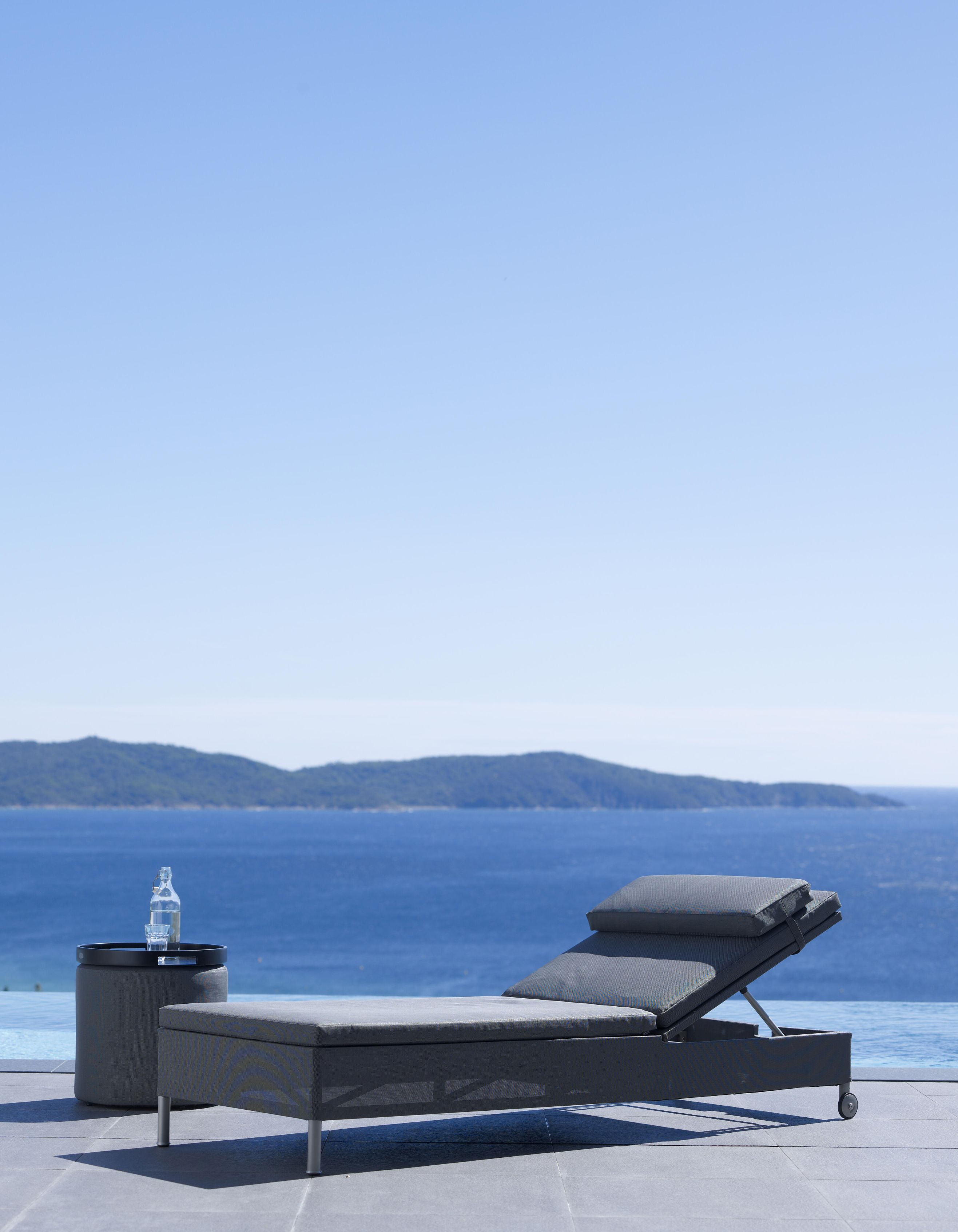 Cane-Line Rest Sonnenliege in Grau mit Beistelltisch und Meerblick für entspannte Stunden.