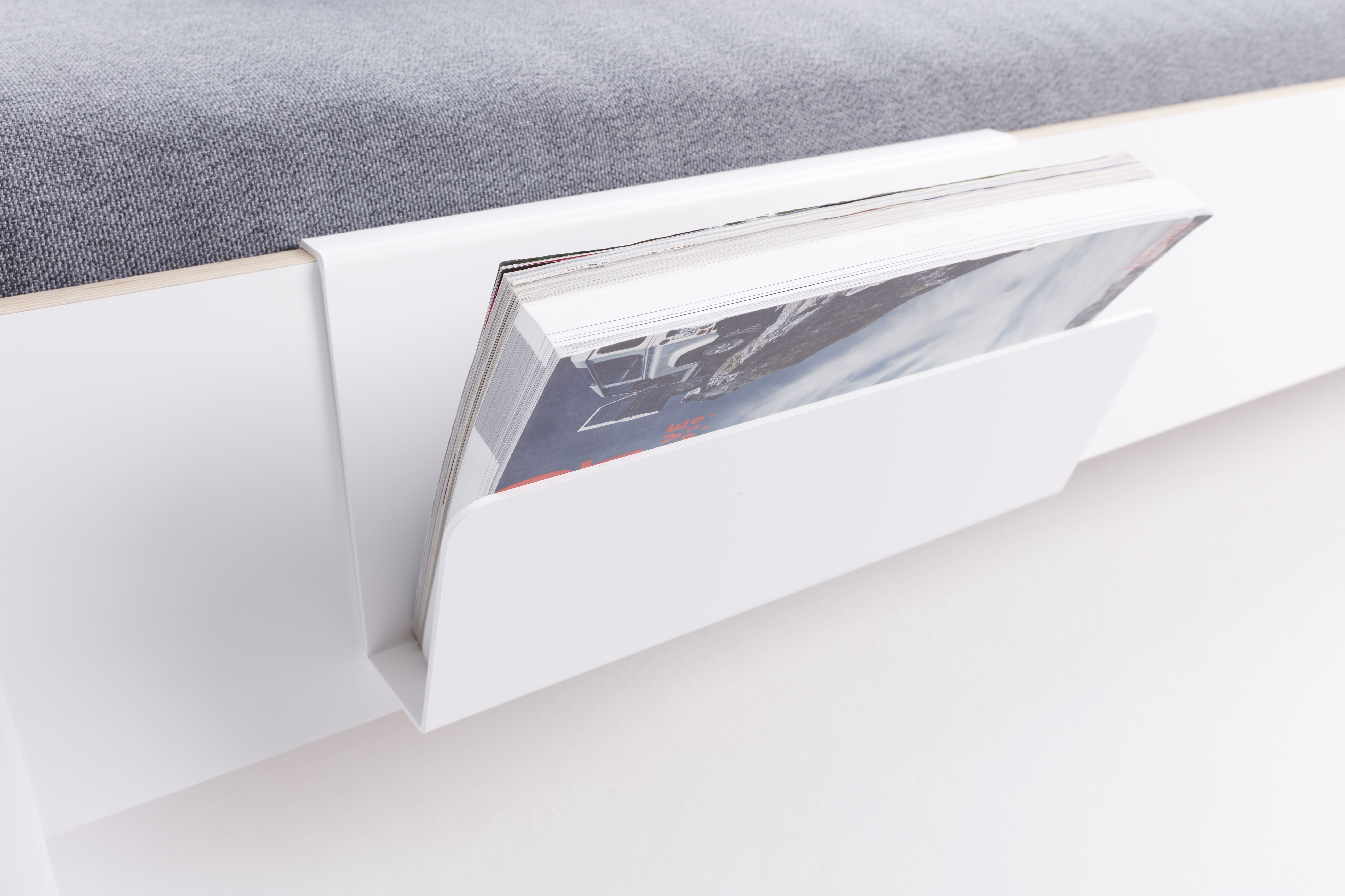 Weiße Zeitschriftenablage für Flai Bett von Müller Möbelwerkstätten, befestigt an einem Bett mit grauer Matratze.