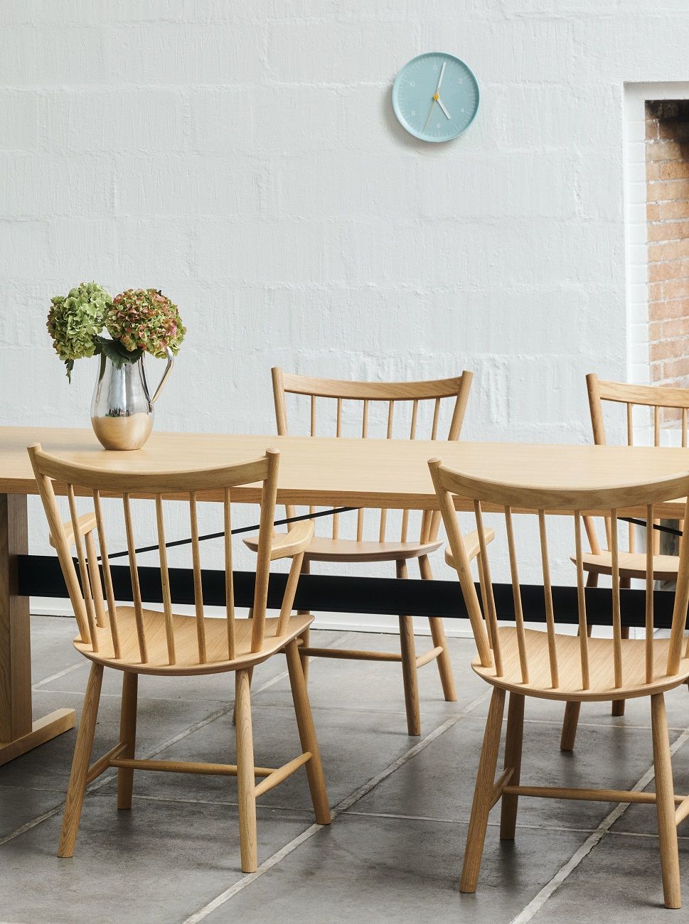 Helles Esszimmer mit Holztisch, Stühlen und einer blauen Hay Wall Clock Wanduhr an der weißen Wand.