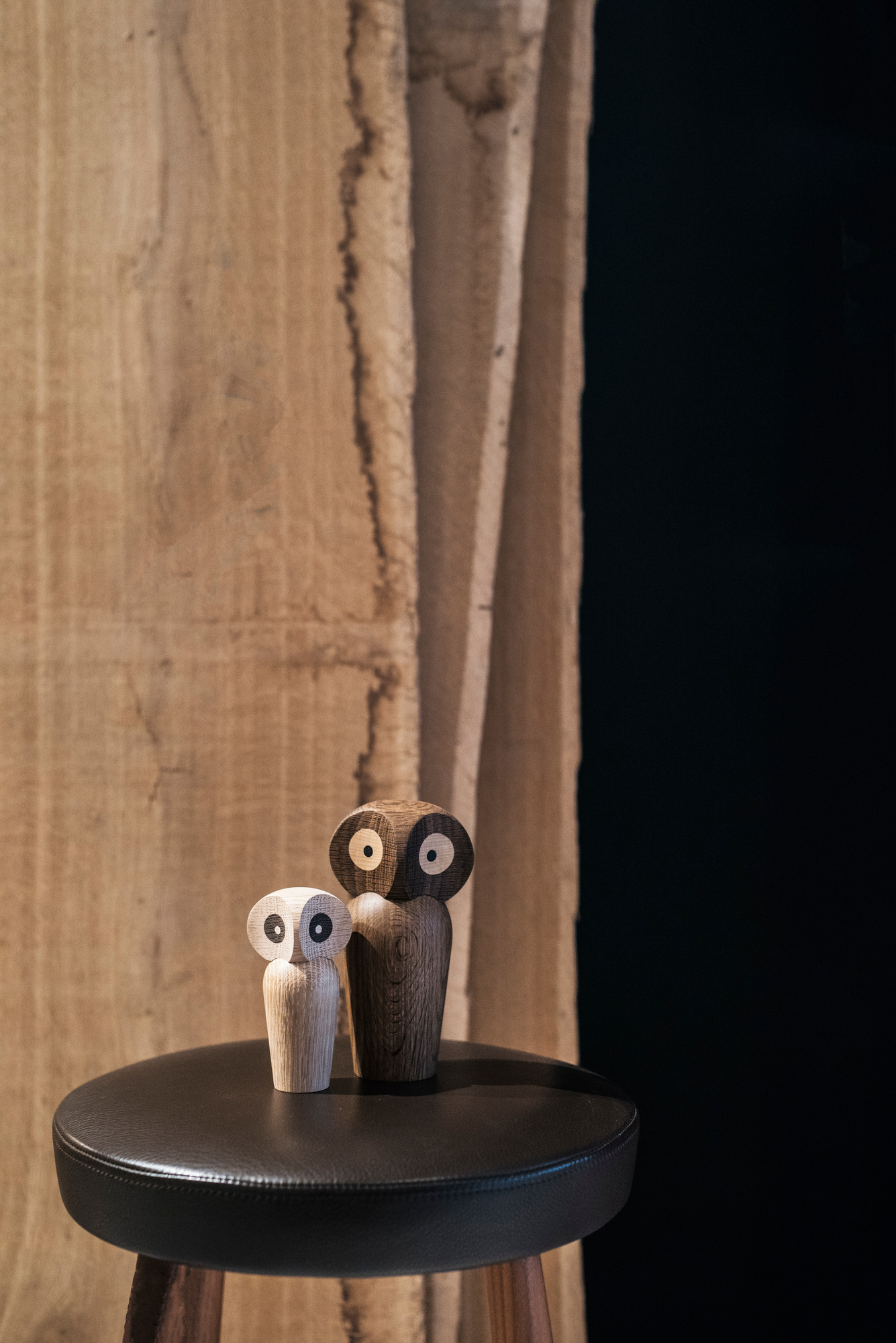 Zwei Architectmade Holzfiguren Eulen, hell und dunkel, als Deko-Objekt auf einem Hocker.