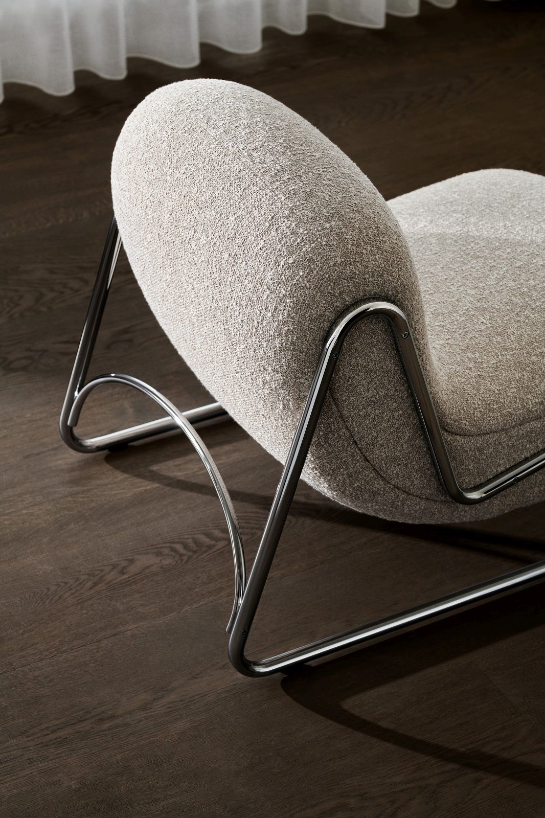 Detailaufnahme: NORR11 Sessel mit beigem Stoffbezug und verchromtem Metallgestell auf dunklem Holzboden.