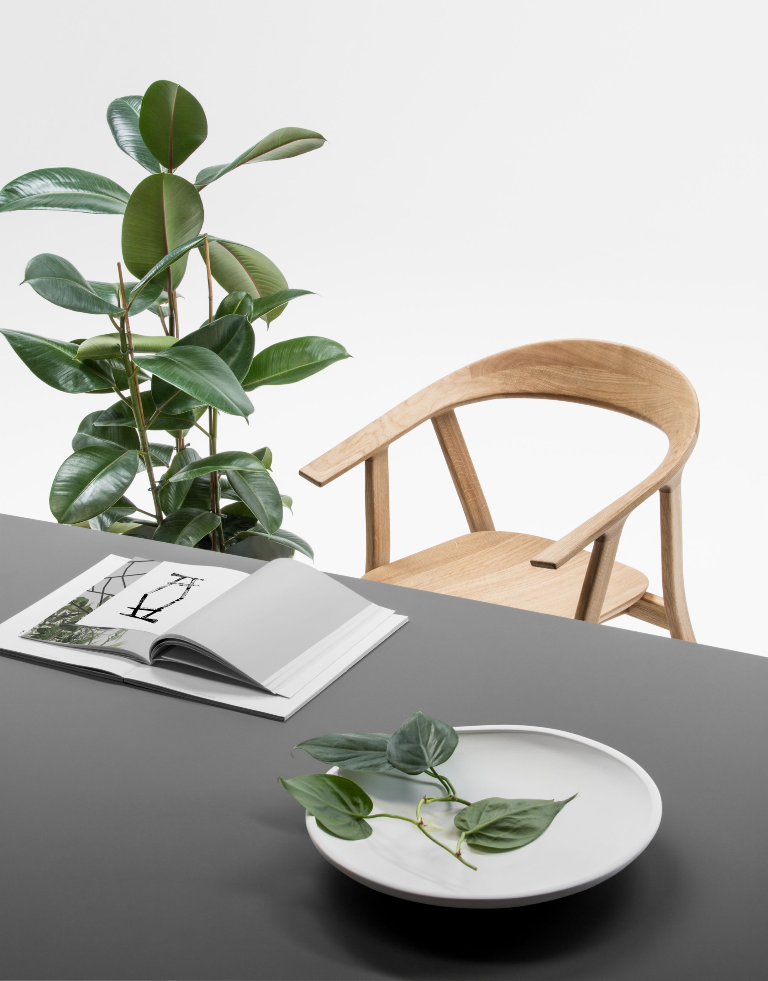 Rhomb Tisch von Prostoria mit Holzstuhl, Pflanze und Dekoration auf grauer Tischplatte.