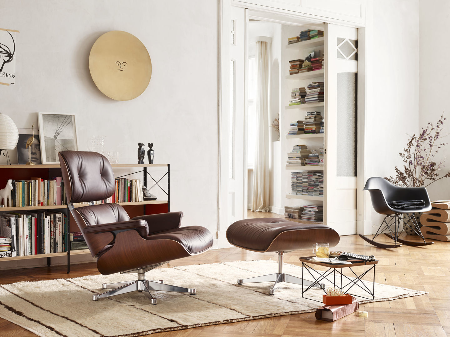 Wohnzimmer mit braunem Eames Sessel mit Sitzpolster und schwarzem Eames Schaukelstuhl im Hintergrund.