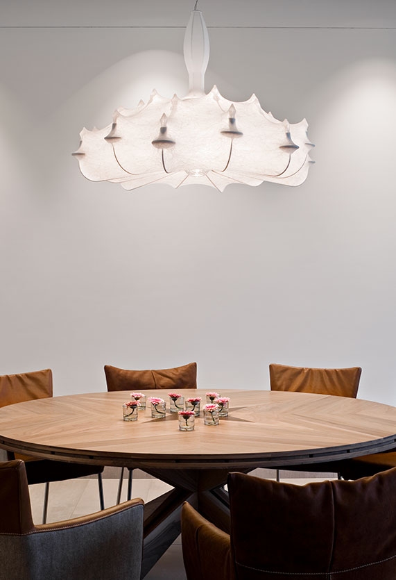 Weiße Flos Zeppelin Hängeleuchte über Esstisch mit Blumen, elegante Innenarchitektur und stimmungsvolle Beleuchtung.