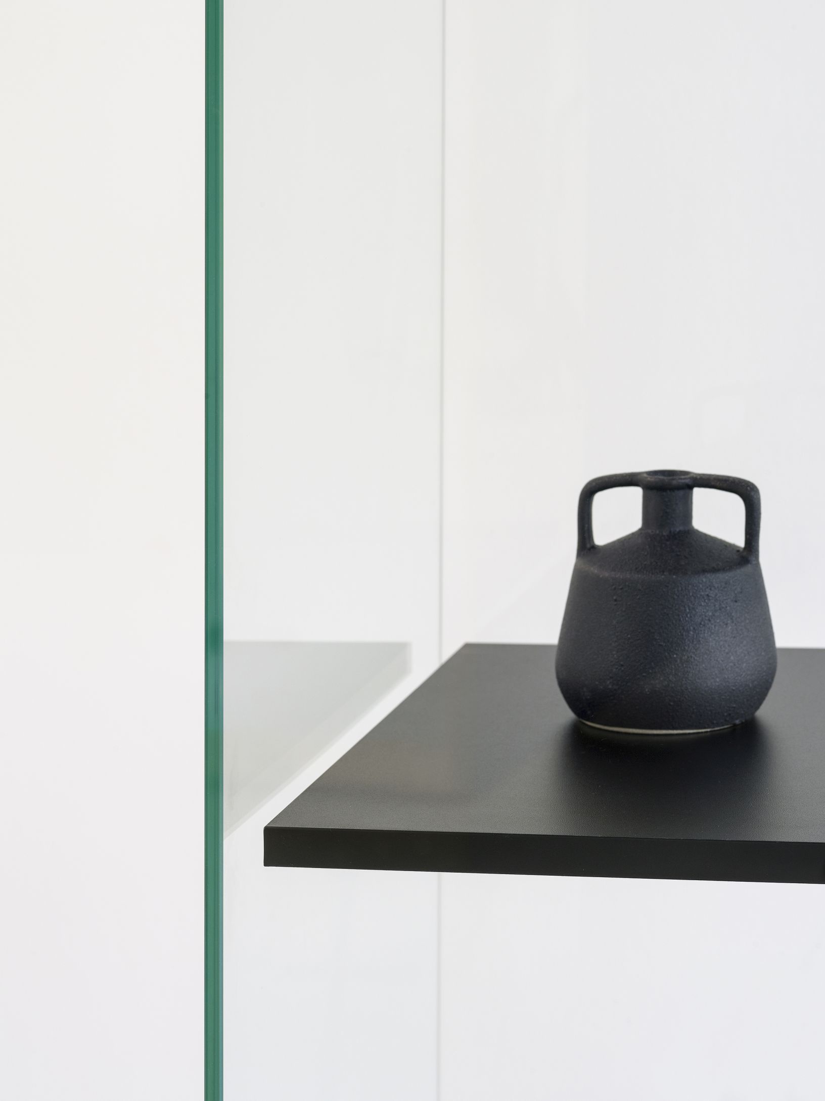 Detailaufnahme einer Stolp Vitrine mit schwarzer Keramikvase auf einem Regalbrett.
