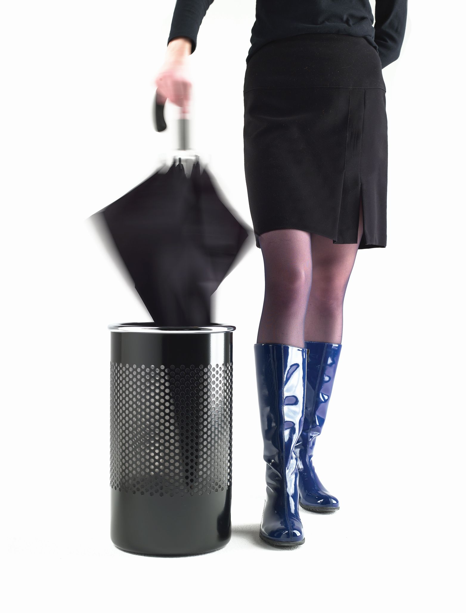 Frau wirft Schirm in Cribbio Schirmständer/Papierkorb. Designobjekt für Büro und Zuhause. Schirmständer aus Metall.