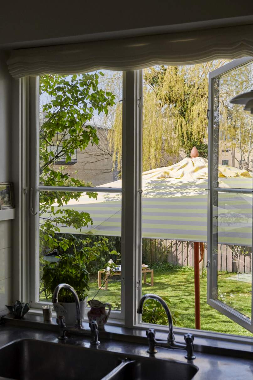 Blick aus dem Fenster auf einen Messina Sonnenschirm von Skagerak mit gelben Streifen im Garten.