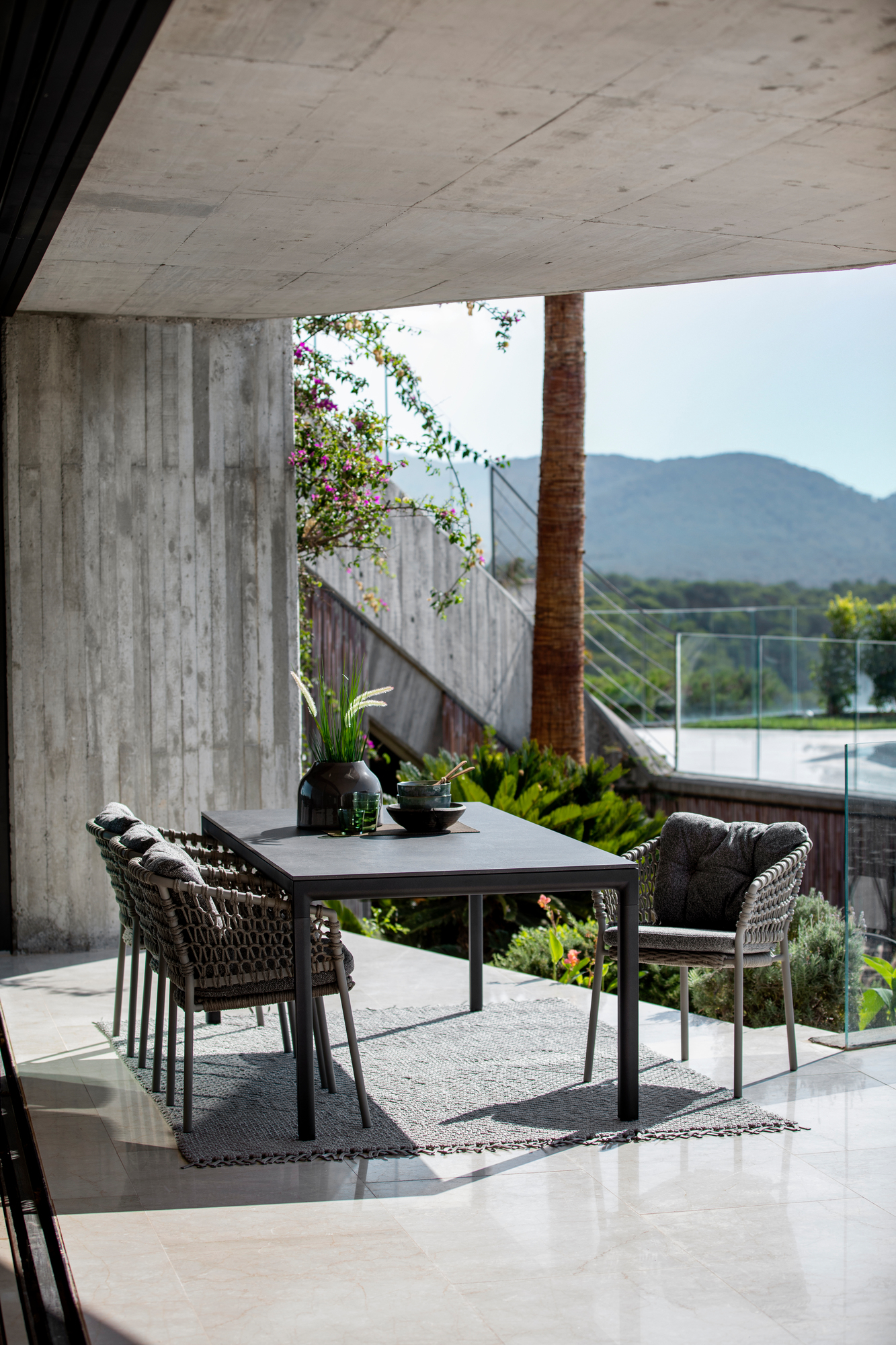 Dunkelgrüne Cane-Line Ocean Outdoor Sessel aus Rattan mit Esstisch auf einer Terrasse.