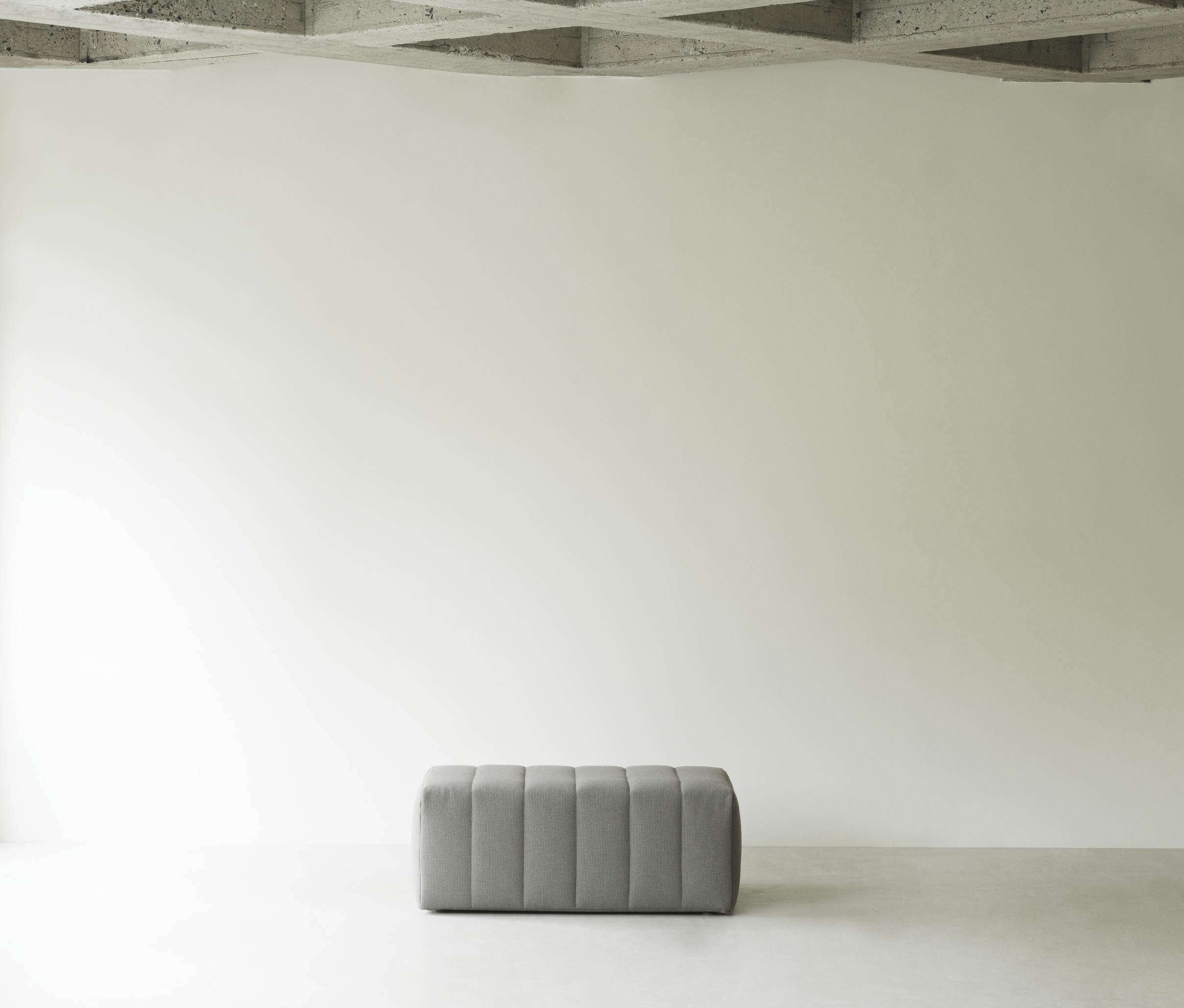 Grauer Scene Pouf Hocker von Normann Copenhagen vor heller Wand. Sitzhocker für Wohnzimmer.