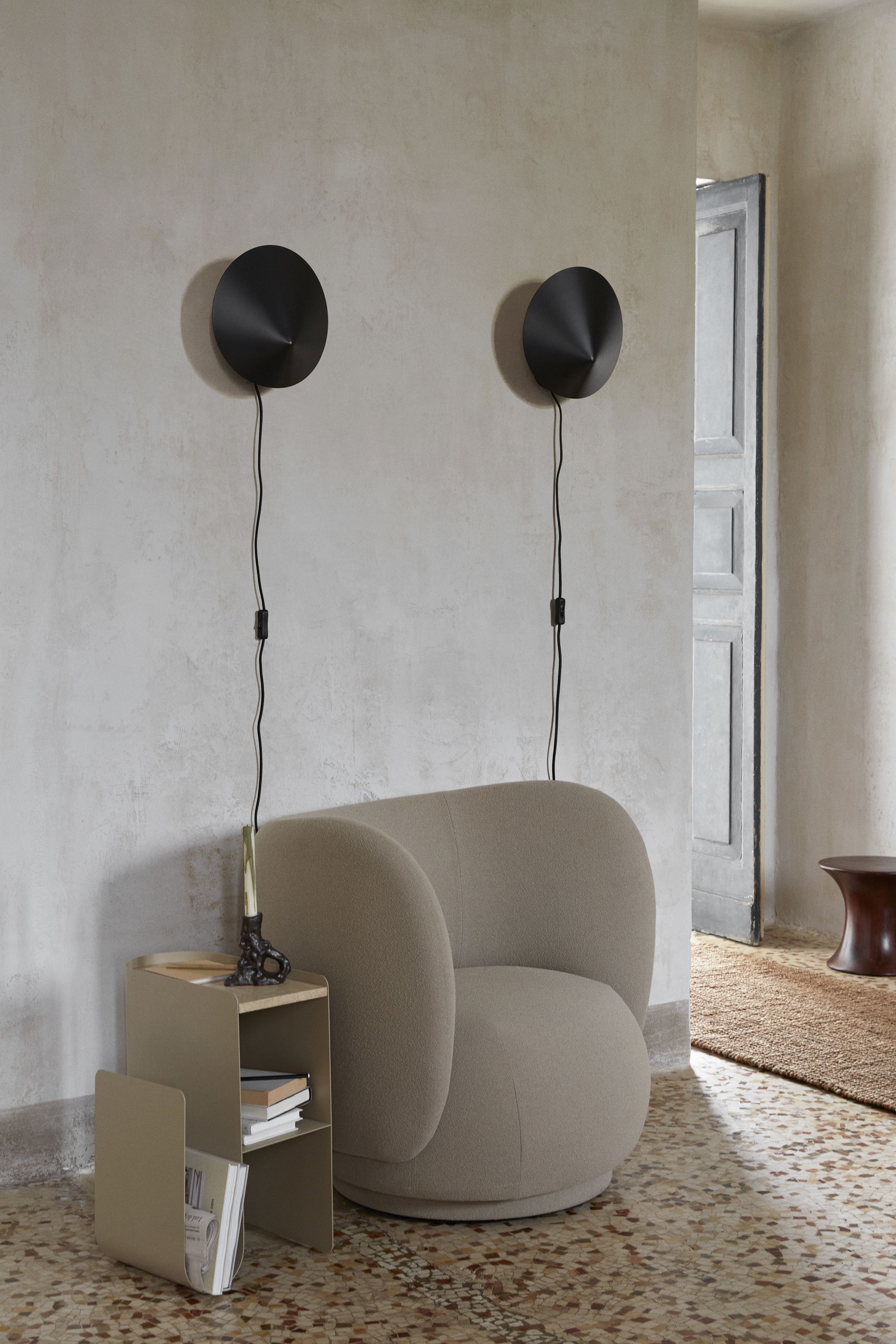 Zwei schwarze Arum Wandleuchten von Ferm Living über einem Sessel und Beistelltisch.