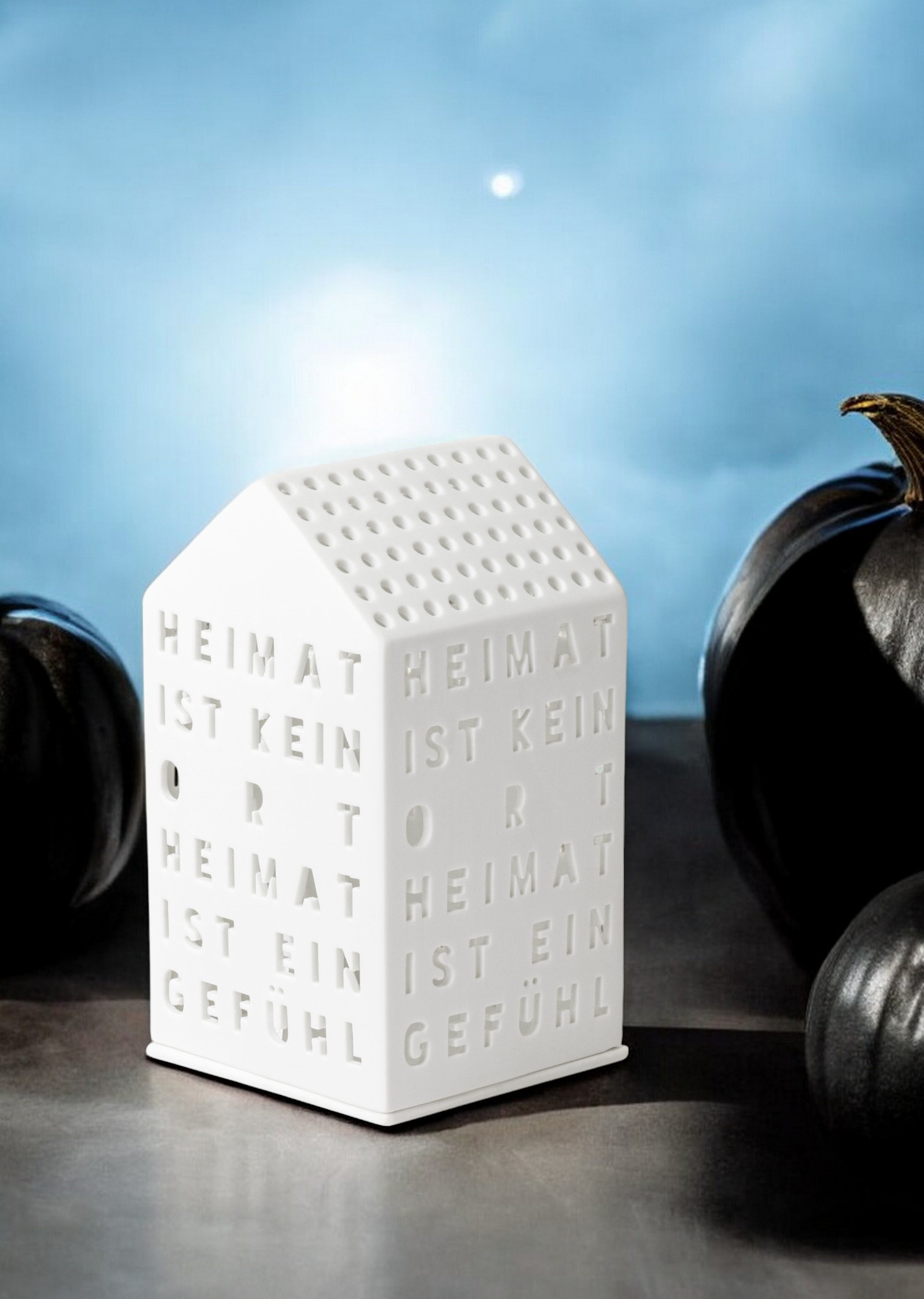 Weißes Lichthaus "Heimat ist kein Ort" von Räder mit Schriftzug und Lochmuster, stimmungsvolle Dekoration.