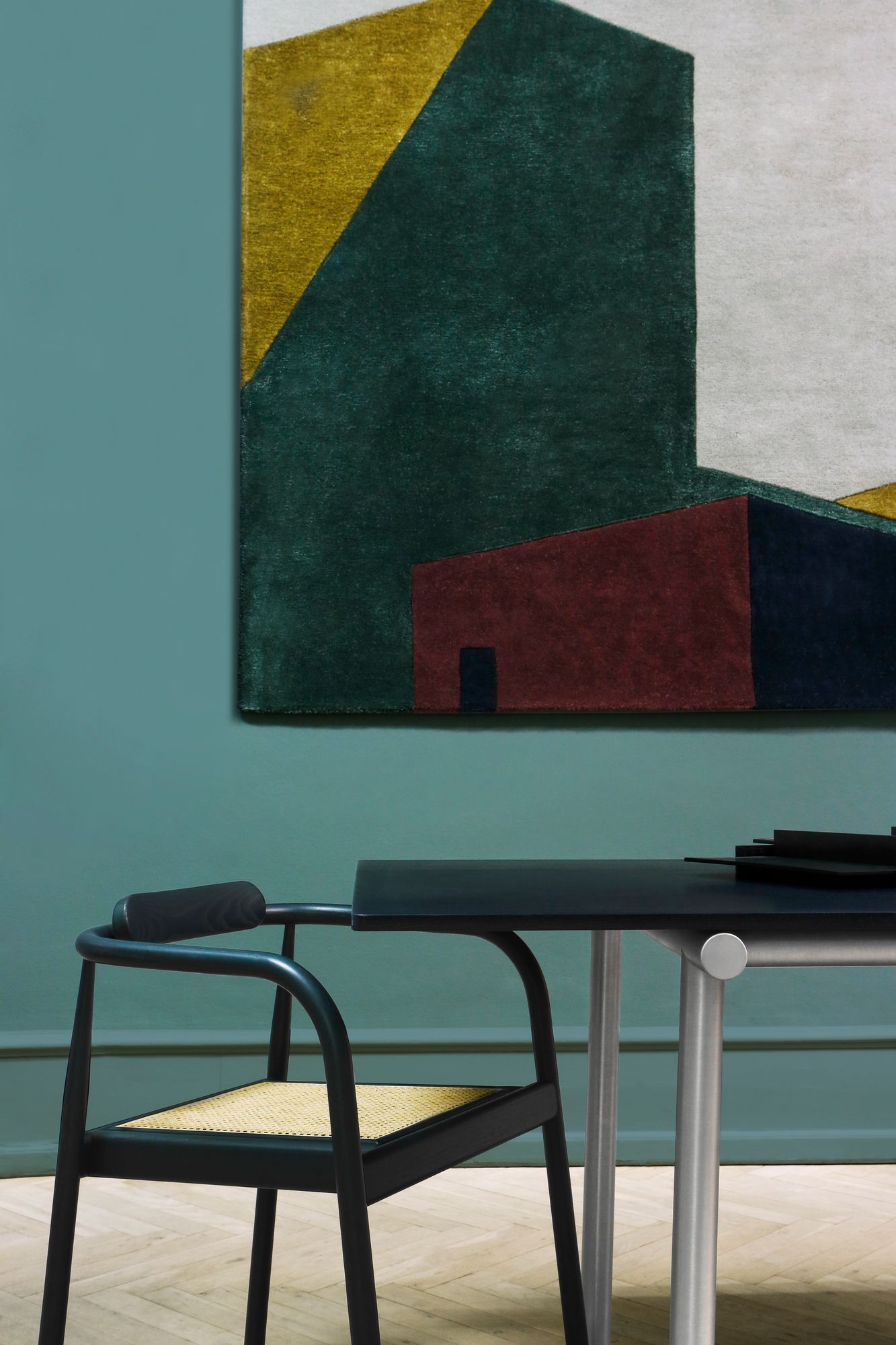 Arqui Teppich mit geometrischem Muster in Grün, Gelb und Rot an grüner Wand.