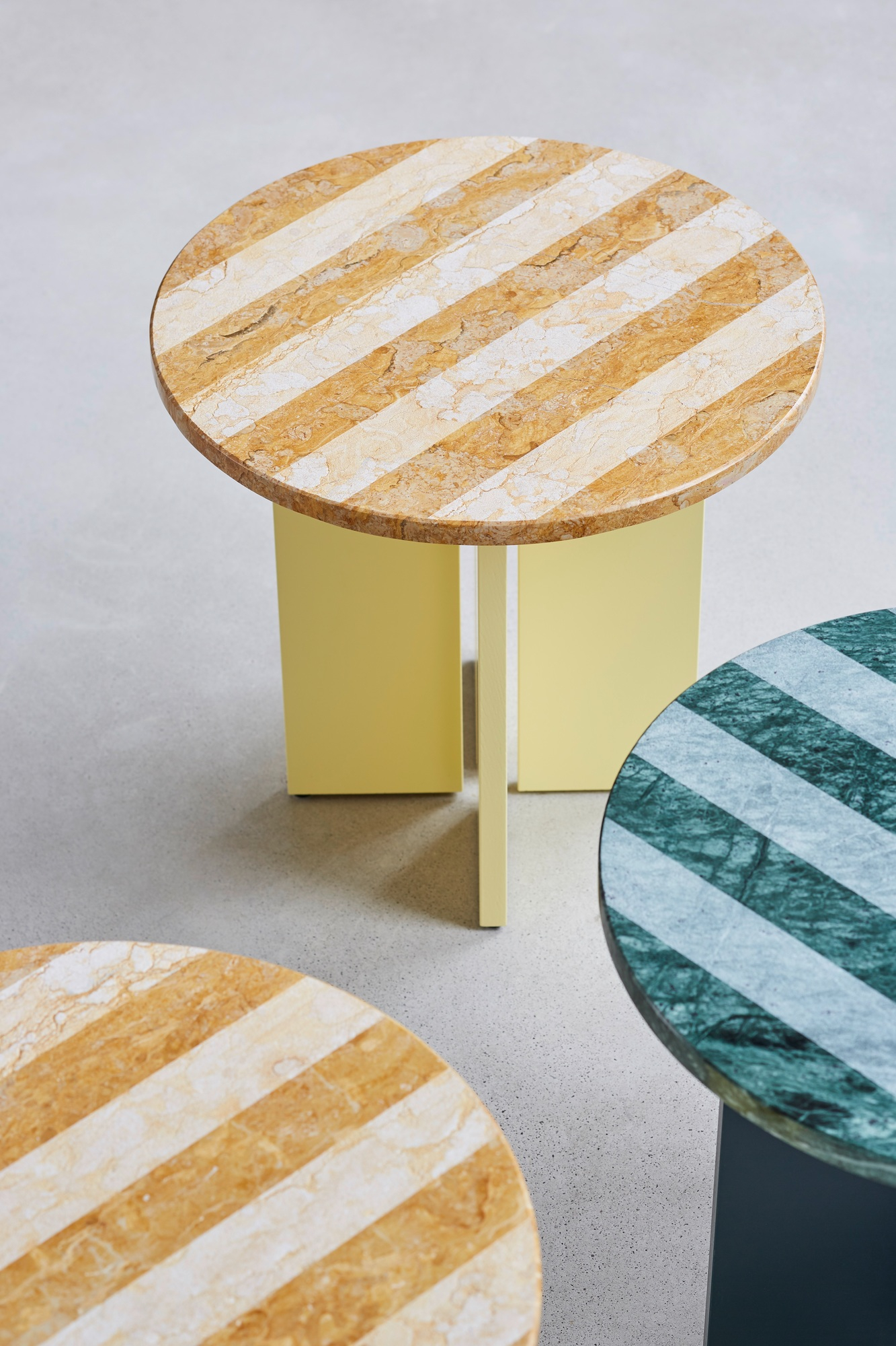 Sediment Beistelltisch mit runder Marmorplatte und gelbem Gestell, weitere Tische mit Marmor sichtbar.