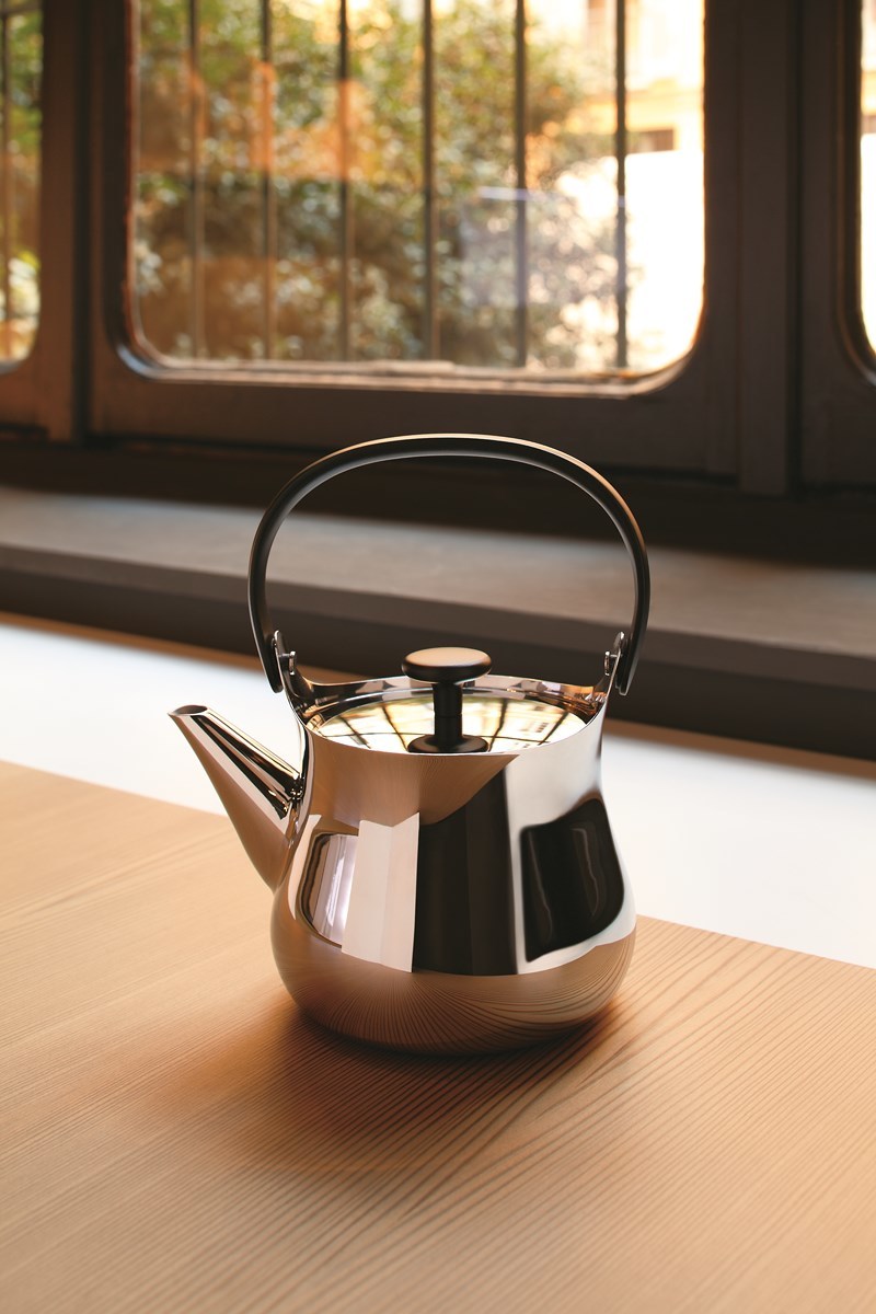 Nahaufnahme der glänzenden Alessi Teekanne "Cha" aus Edelstahl vor einem Fenster.