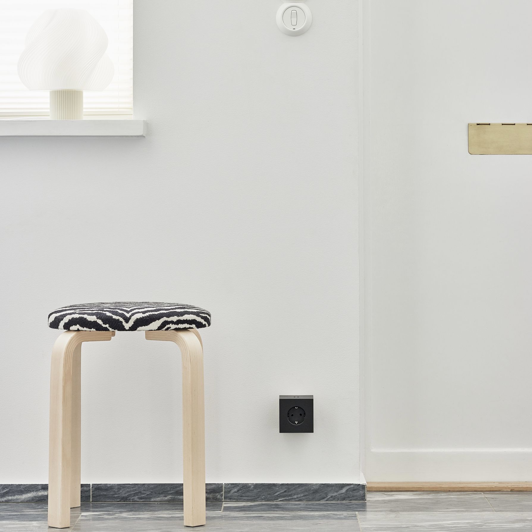 Schwarzer Avolt Square 2 Steckdosenwürfel mit USB-C an weißer Wand neben Hocker.