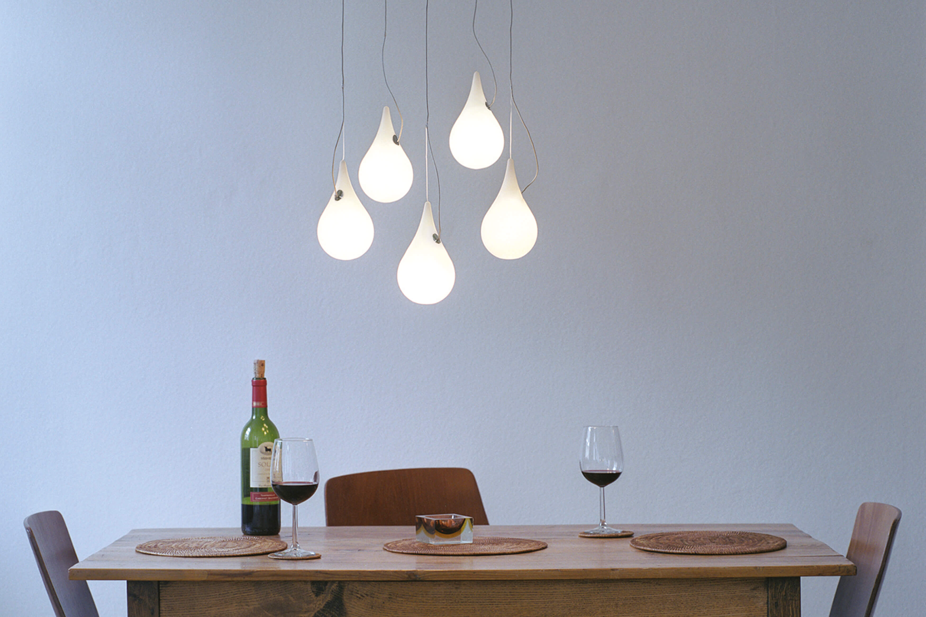 Liquid Light Pendelleuchte: Tropfenförmige Designerlampe über Esstisch mit Wein und Gläsern.