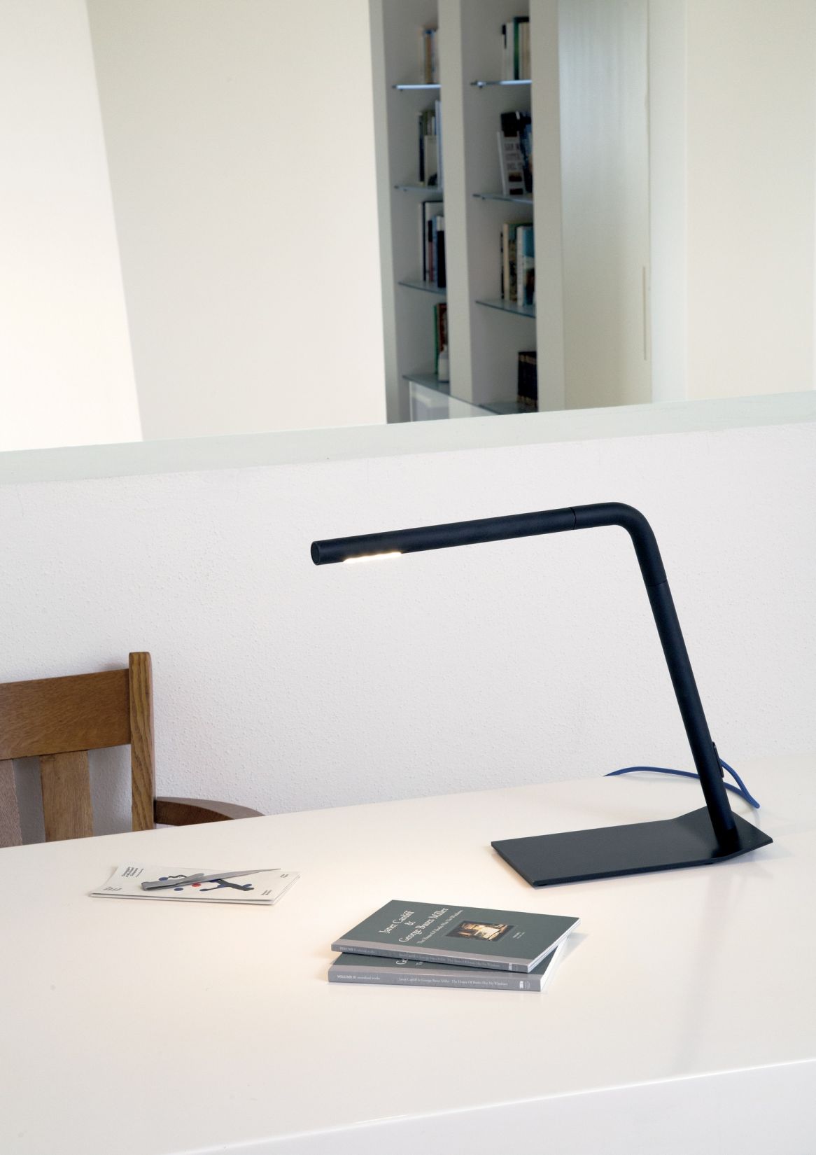 Schwarze Colibrì Tischleuchte von Martinelli Luce auf einem weißen Tisch mit Büchern. Designlampe.