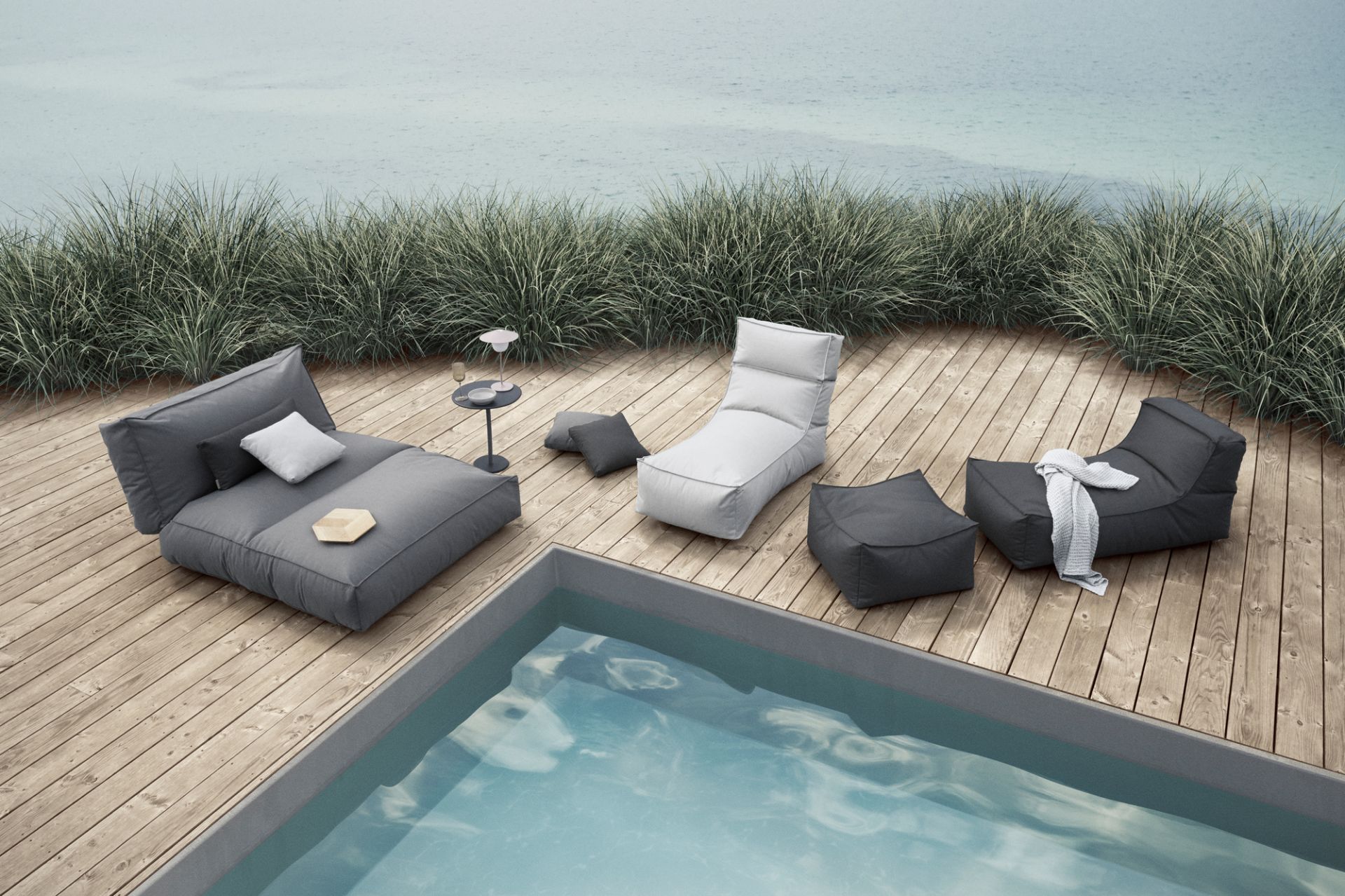 Graue und weiße Outdoor-Lounge-Möbel aus Stoff auf Holzdeck neben Pool und Meer.
